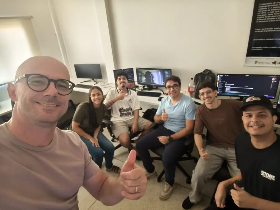 Sete integrantes do LEDS reunidos no laboratório, com o banner institucional do laboratório na parede ao fundo