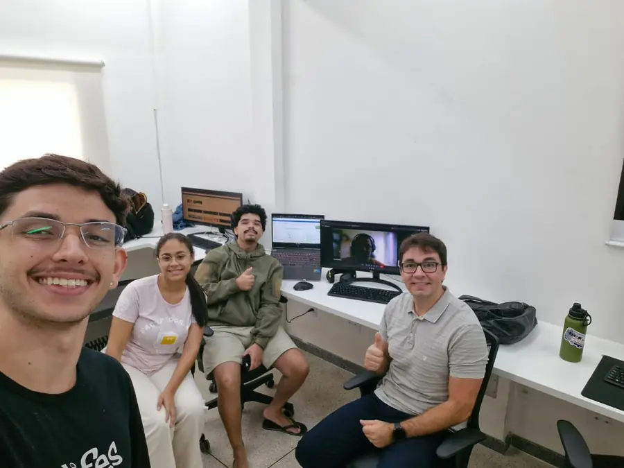 Quatro integrantes do LEDS sentados junto às estações de trabalho, com uma videochamada aberta no monitor