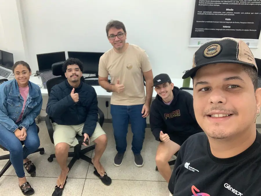 Cinco integrantes do LEDS na sala de trabalho, diante do painel com a missão, a visão e os valores do laboratório