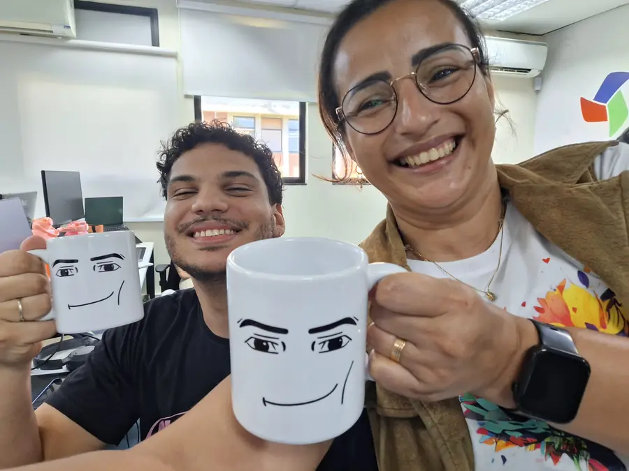 Duas pessoas sorriem segurando canecas personalizadas do LEDS