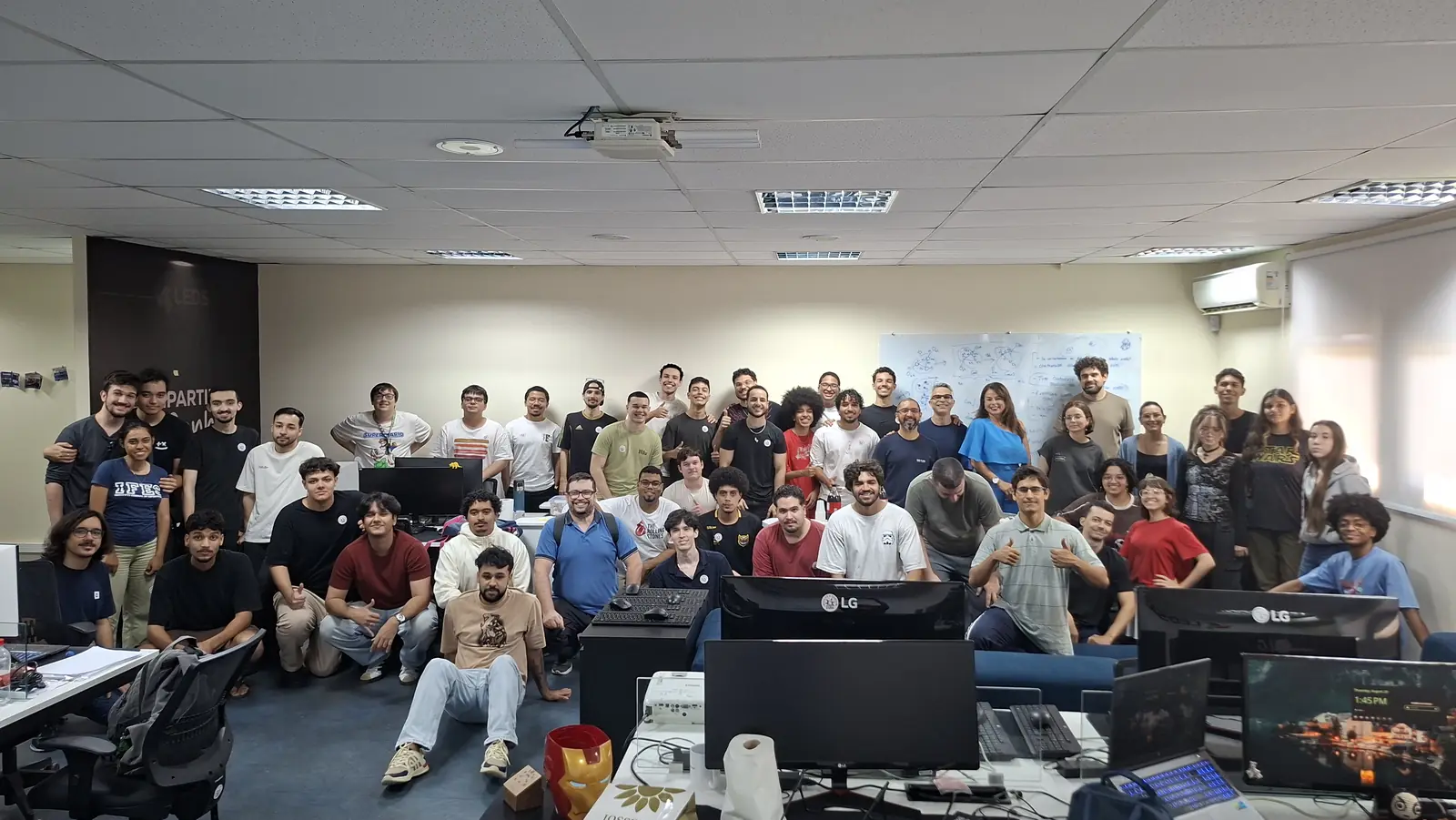 Grupo numeroso posa entre as estações de trabalho do laboratório
