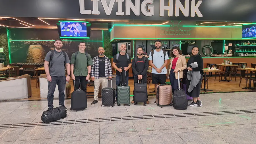 Oito integrantes com malas posam no saguão do aeroporto de madrugada
